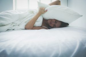 Young woman covering her head and ears with pillows.